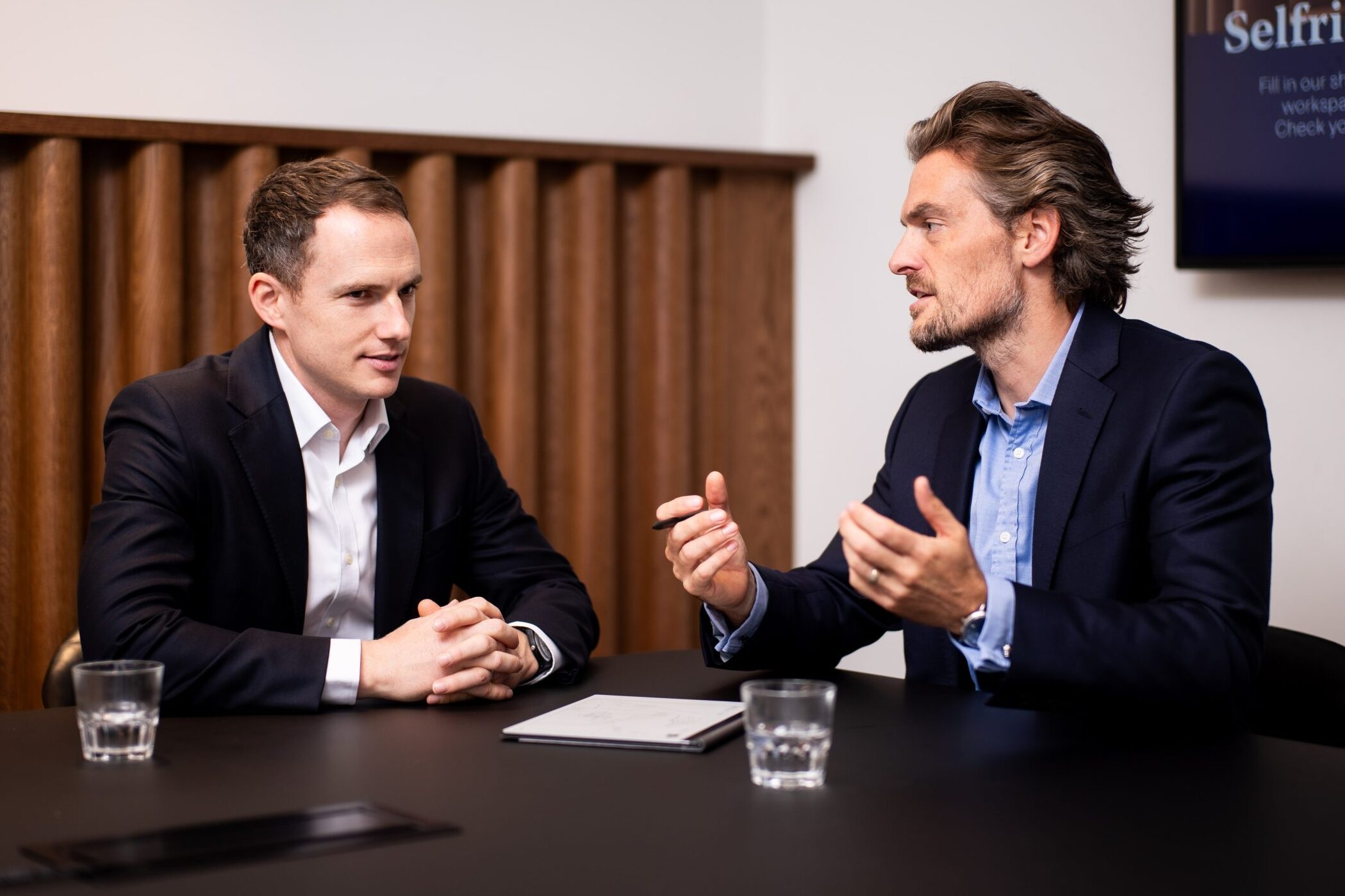 Two men sitting at a table talking to each other about finance.